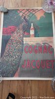 Full view of the original Cognac Jacquet advertising poster showing a peacock next to a bottle of cognac with vibrant colors and the brand name in red.