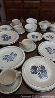 Overall group showing various plates, bowls, cups, saucers and cream/sugar bowl in Pfaltzgraff Yorktown pattern with blue floral motif on white ceramic stoneware.