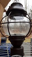 Close-up image of the top and globe of the post lamp in rustic bronze finish with metal cage and glass globe.