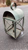 Full view of the green patina post lantern with glass panel and metal bars on other sides, sitting on pavement.