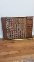 Front view of the wooden scoreboard with all slots and paper number cards visible, showing condition and detail.