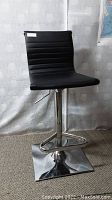 Side view showing black padded backrest and seat, chrome footrest bar and square base