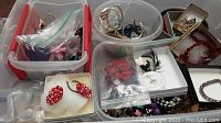 Overview of tote with multiple containers filled with costume jewelry including earrings, bracelets, brooches, and necklaces. Includes a mix of metal, enamel, beads, and feathered pieces.