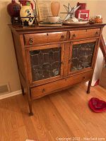 Front view of closed oak cabinet showing leaded glass doors and brass hardware with objects on top