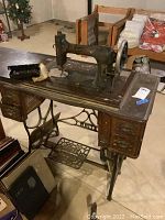 Full view of antique White Rotary sewing machine mounted on wooden cabinet with cast iron treadle base. Shows surface wear, rust, and general aged condition.
