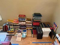 Full view of the entire collection of books showing stacks of various titles and genres on a wooden floor corner.