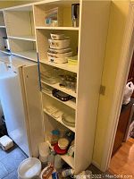 Tall shelving unit with assorted kitchenware including Corning Ware casseroles, glass jars, plastic containers, and utensils.