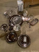 Full view of assortment of silverplate platters, glassware including boxed Mikasa vase, candlesticks, and anniversary pieces.