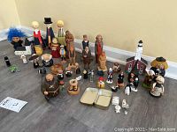 Photo showing a group of assorted carved and painted wooden figures, including friars, a troll doll with blue hair, penguins, and other characters in various sizes from 1 to 9 inches tall.