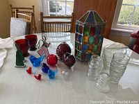 Overall lot on table showing stained glass candle shade, glass birds, apples, perfume bottle, oil lamp, glass planters, stained glass figurines