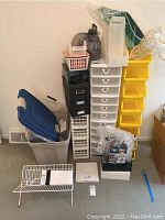Photo showing stacked white and yellow plastic drawers, various plastic bins and totes, vacuum bags, and some boxed items arranged against a wall.