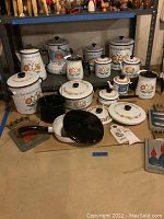 Full overview of enamelware items including coffee percolator, canisters, saucepan, pitcher and filter basket on floor