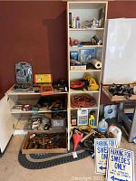 Wide shot of tools and automotive liquids on shelves and floor, including extension cords, socket wrench kit, staple gun, storage cabinets, funnel, and car fluids. Mini fridge visible but not included.