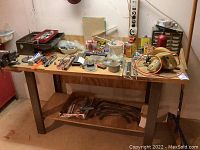 Wide angle showing wooden workbench with assorted hand tools, metal toolbox, organizer with small drawers, and various small hardware items scattered on top.