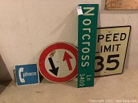 Four vintage metal signs grouped together showing a blue phone sign, round two-way traffic sign, green Norcross street sign, and speed limit sign.