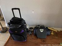 View of lot items including black and purple wheeled travel case, digital scale, air mattress, brass desk lamp, and electrical items.