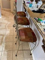 Side view of three metal frame bar stools with patterned upholstered seats and backs lined up along a kitchen counter.