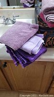 Stack of purple towels on a bathroom countertop next to a sink and mirror