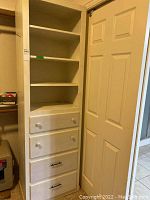 Photo of tall white wood cabinet, showing four shelves and four drawers with mixed hardware pulls.