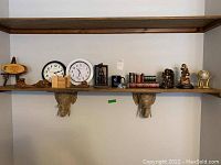 Wide view of two wooden shelves displaying two alarm clocks, assorted decorative bookends, small globe figurine, faux books, and other small decorative items.