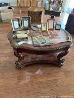 Front view of carved wooden coffee table with picture frames and items on top, showing ornate legs and lower shelf.