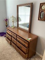 Front and side view of wooden dresser with nine drawers and attached mirror in a carpeted room.