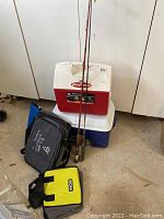 Wide view of fishing rods, reels, hard wall coolers, and soft wall coolers placed on the floor.