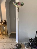 Full view of the floor lamp showing metal base, pole, and Tiffany style stained glass shade.