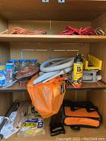 Cabinet interior showing extension cords on the top shelf, jars with nails and screws, hoses, and other tools and accessories on lower shelves.
