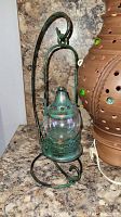 Small green metal lantern with glass globe and metal stand on a granite counter.