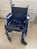 Front angled view of blue frame Empower lightweight wheelchair with black fabric seat and attached foot pieces.