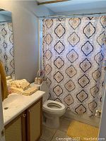 Bathroom scene showing shower curtain, yellow towels folded on counter, trash can near toilet