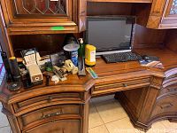 Wide view of wooden desk with monitor, keyboard, mouse, and various office supplies arranged around.