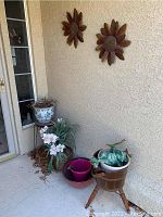 View showing the wooden tripod plant stands, pots including the ceramic floral pot, pink and red plastic pots, faux orchid flowers, and decorative green frog figurine.