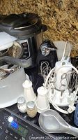 Photo showing Instant Pot, countertop mixer, salt & pepper shakers, plastic food container lids, and electric can opener grouped on countertop.