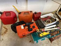 Orange and small red gas cans visible behind cordless drill case and toolbox