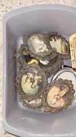 Top view of ornate vintage oval picture frames inside a plastic tote, showing different classical portrait images.