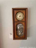 Front view showing the full rectangular wooden framed wall clock with circular dial and oval floral display below.