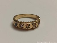 Front view of the gold ring showing 5 colored stones set in star-shaped cutouts around the band and beaded edge decoration.