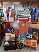 Shelf with assorted books including cookbooks, dictionaries, encyclopedias, with puzzles and games below