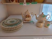 Overview of Sadler teapots, creamer, sugar set, Royal Doulton Oakland plates, and Saji ceramic trivet on display.