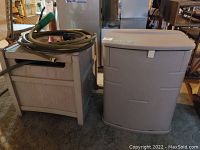 Two small deck boxes side by side indoors, one Rubbermaid and one Suncast, light tan colors, some wear visible.