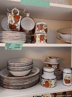 Overview of stacked dinner plates, bowls, mugs, saucers, creamer, sugar bowl and salt shaker on shelving.