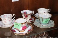 Five assorted vintage tea cups and saucers on display with floral and gold accents