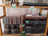 Shelf showing stacked Technics stereo receiver SA-160, cassette deck RS-B105, Insignia CD player, along with CDs and cassette tapes in holders.