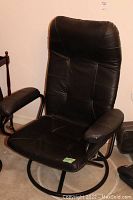 Front angle view of the black vinyl reclining chair showing padded armrests, padded seat and back, circular base.