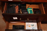 Open wooden drawer with multiple small purses, wallets, travel bag, and travel pillow box visible inside drawer.