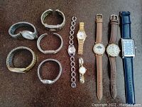 Collection of 11 wristwatches laid out on a surface showing variety of bands and dial styles