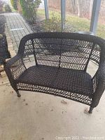 Brown all-weather wicker loveseat on back patio showing open lattice weave pattern.