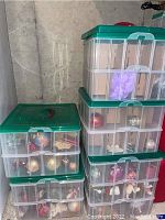 Stack of clear plastic storage tubs with green lids containing various Christmas ornaments, seen from the front view showing the tubs stacked in a corner.